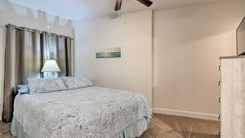 Un dormitorio con cama, ventilador de techo, lámpara, una obra de arte en la pared y un armario de madera.