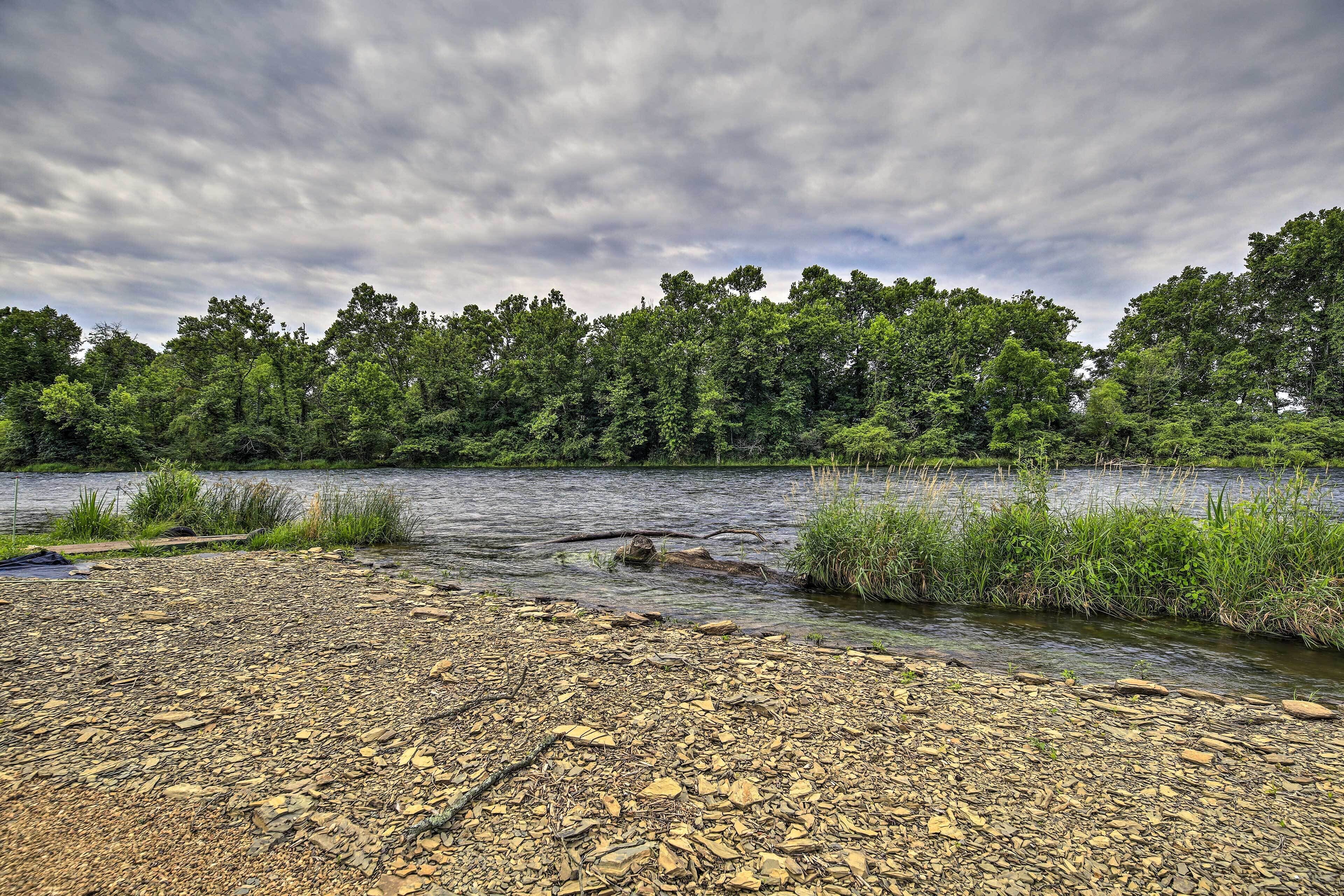 A riverbank with pebbles and a forest in the background.