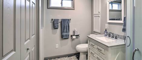 Une salle de bain comprenant des toilettes, un lavabo, un meuble-lavabo et une fenêtre située au-dessus des toilettes.