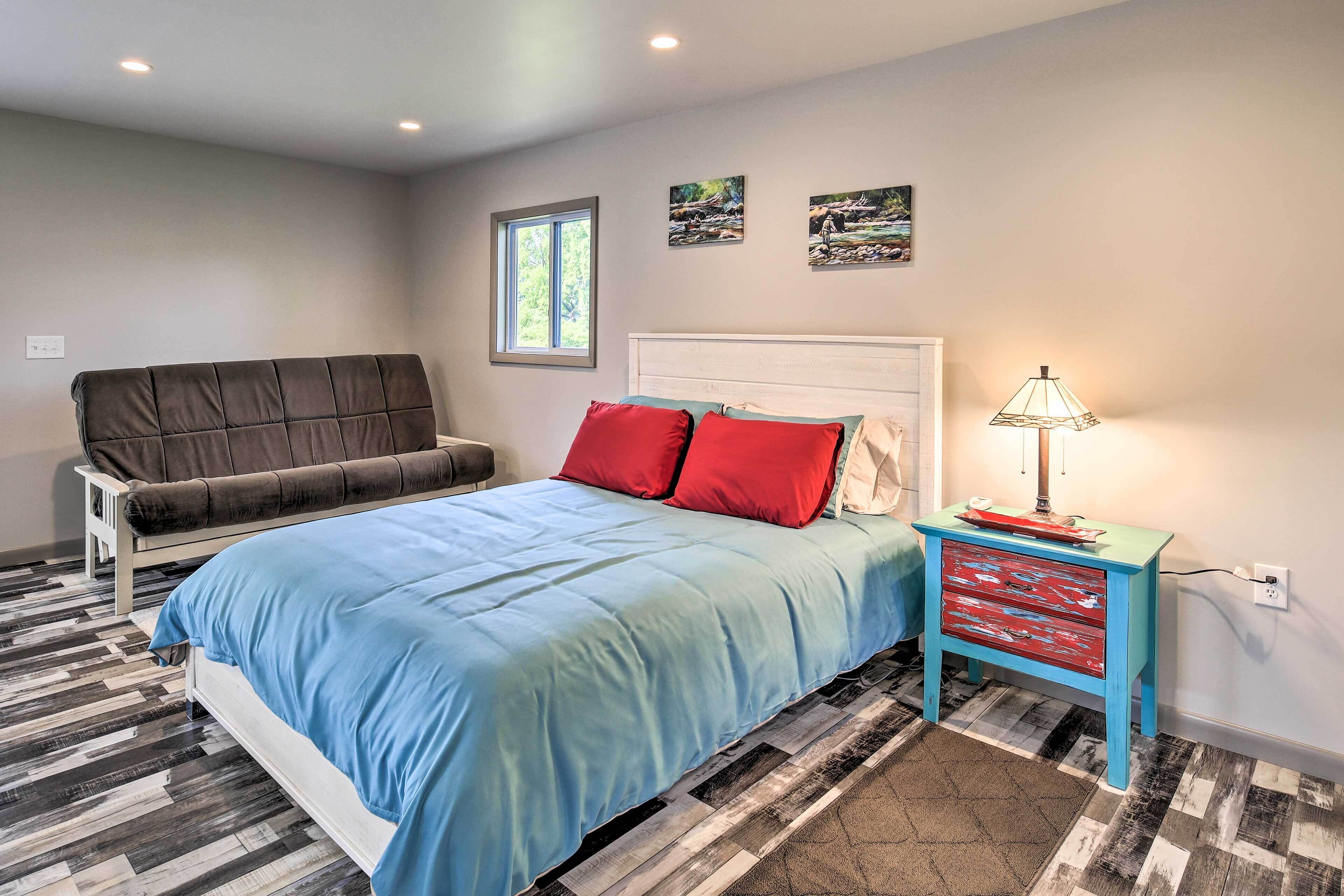 A bedroom with a bed, a sofa, a nightstand, and a window.