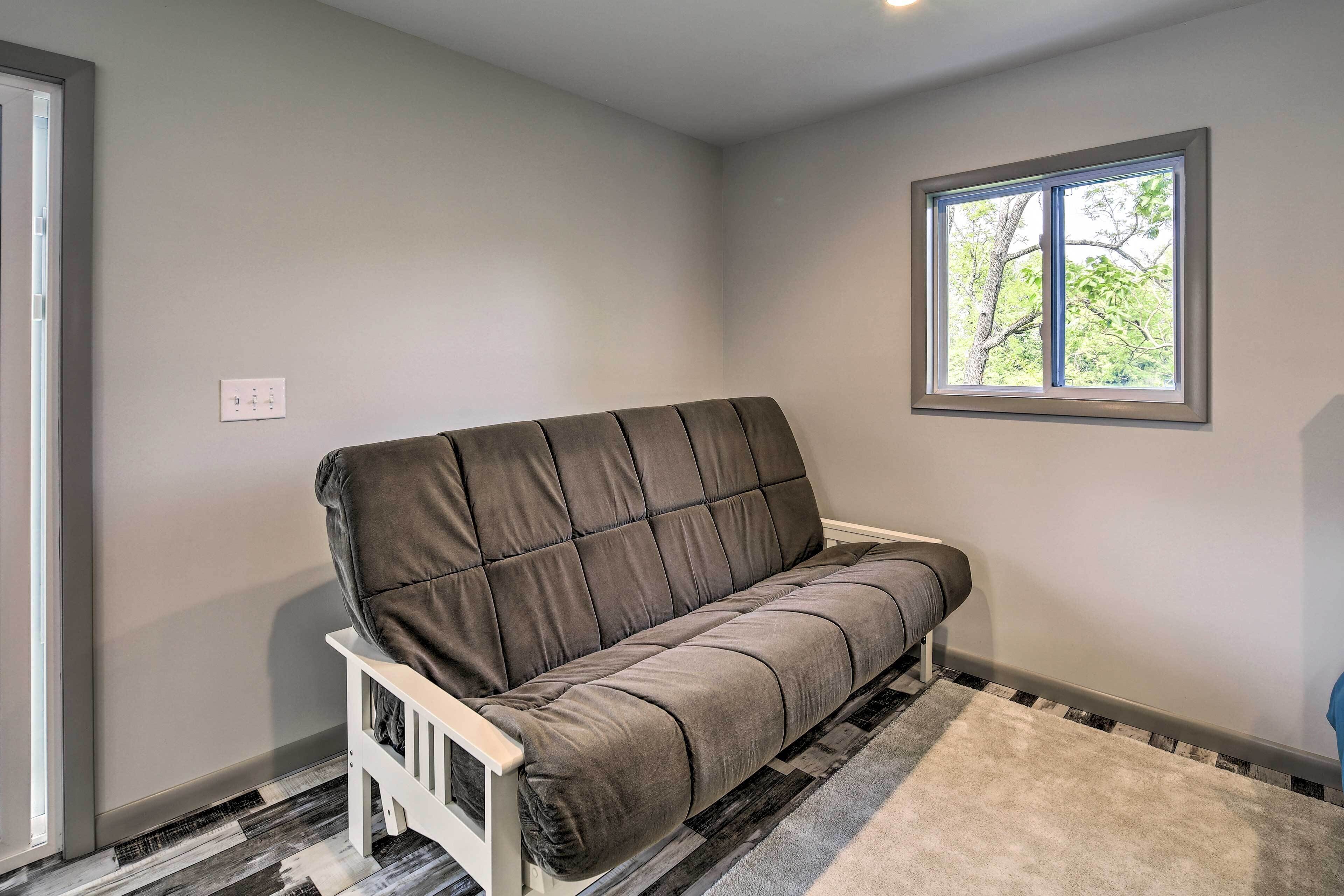 A grey sofa in a corner of a room with a window and a patterned rug.