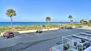 Ein Parkplatz mit Blick auf Strand und Meer, ein Golfmobil und ein rotes Auto.