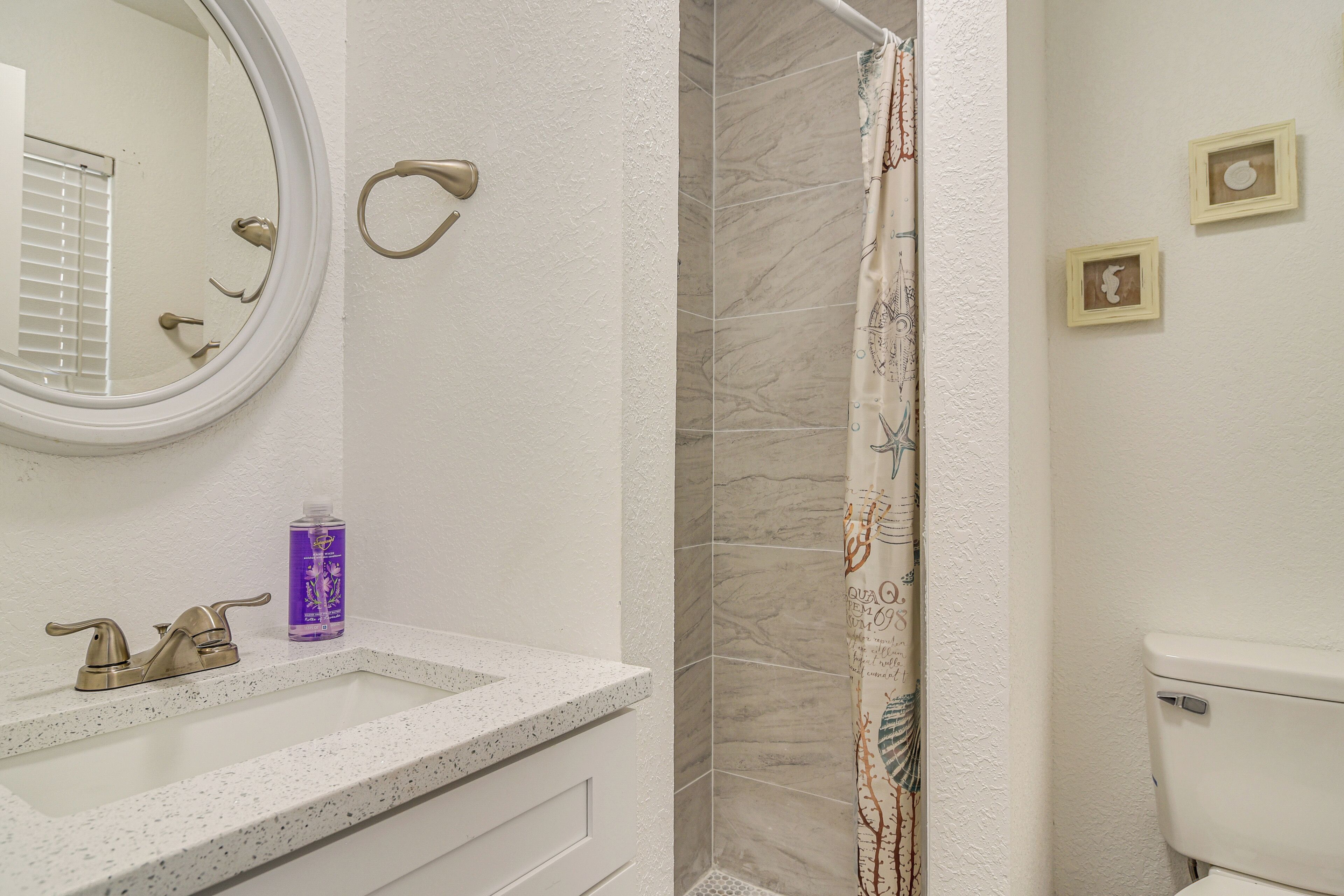 A bathroom with a white sink, a round mirror, a shower with a patterned curtain, and a toilet.