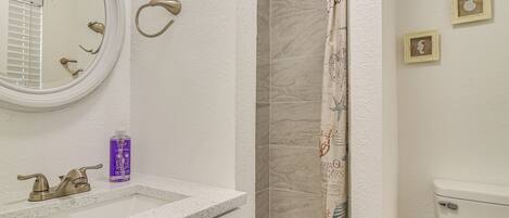 A bathroom with a white sink, a round mirror, a shower with a patterned curtain, and a toilet.