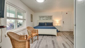 Ein Schlafzimmer mit einem Bett, zwei Korbstühlen, einem Nachttisch, einer Lampe und einem Fenster mit Jalousien.