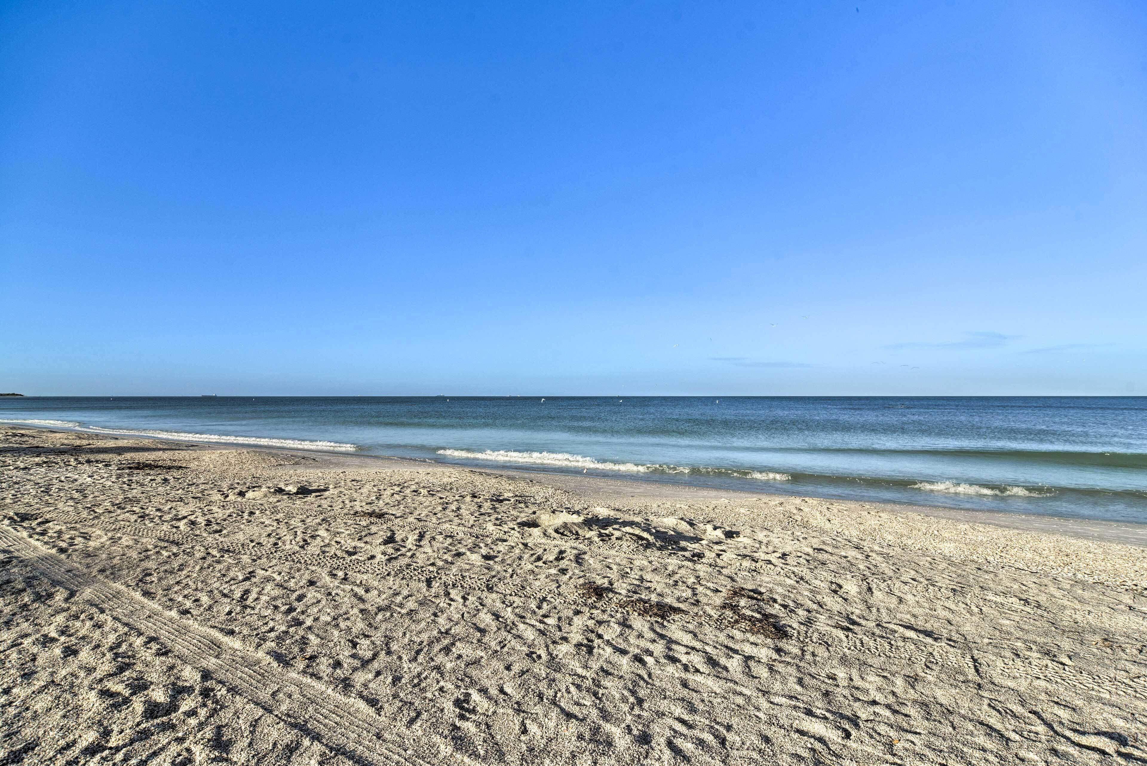 Una playa arenosa con marcas de neumáticos visibles y un cielo azul despejado.