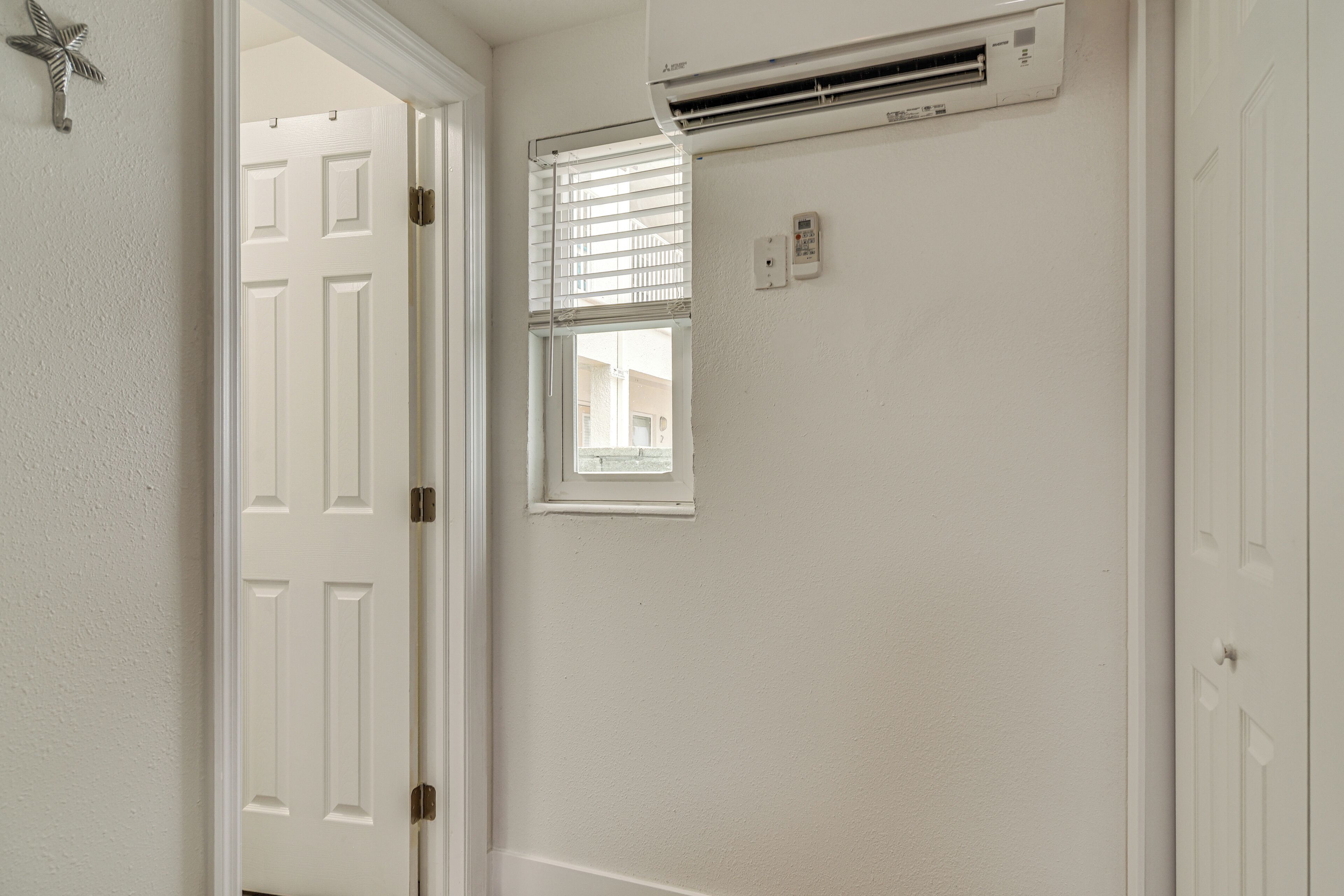 A white door with a cross decoration, an air conditioning unit, and a window with blinds.