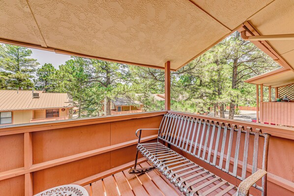 A wooden deck with a bench and a white chair, overlooking a forested area. - Cozy Ruidoso Condo w/ Deck ~ 2 Mi to Cedar Creek! (Ruidoso)