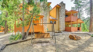A multi-story building with a stone facade, wooden balconies, and a swing set in a forested area. - Cozy Ruidoso Condo w/ Deck ~ 2 Mi to Cedar Creek! (Ruidoso)