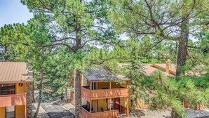A two-story cabin with a balcony, surrounded by pine trees. - Cozy Ruidoso Condo w/ Deck ~ 2 Mi to Cedar Creek! (Ruidoso)