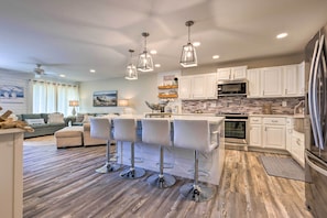 A modern kitchen with white cabinets, stainless steel appliances, and a central island with bar stools. - Bright & Breezy Condo - Walk to Orange Beach! (Orange Beach)