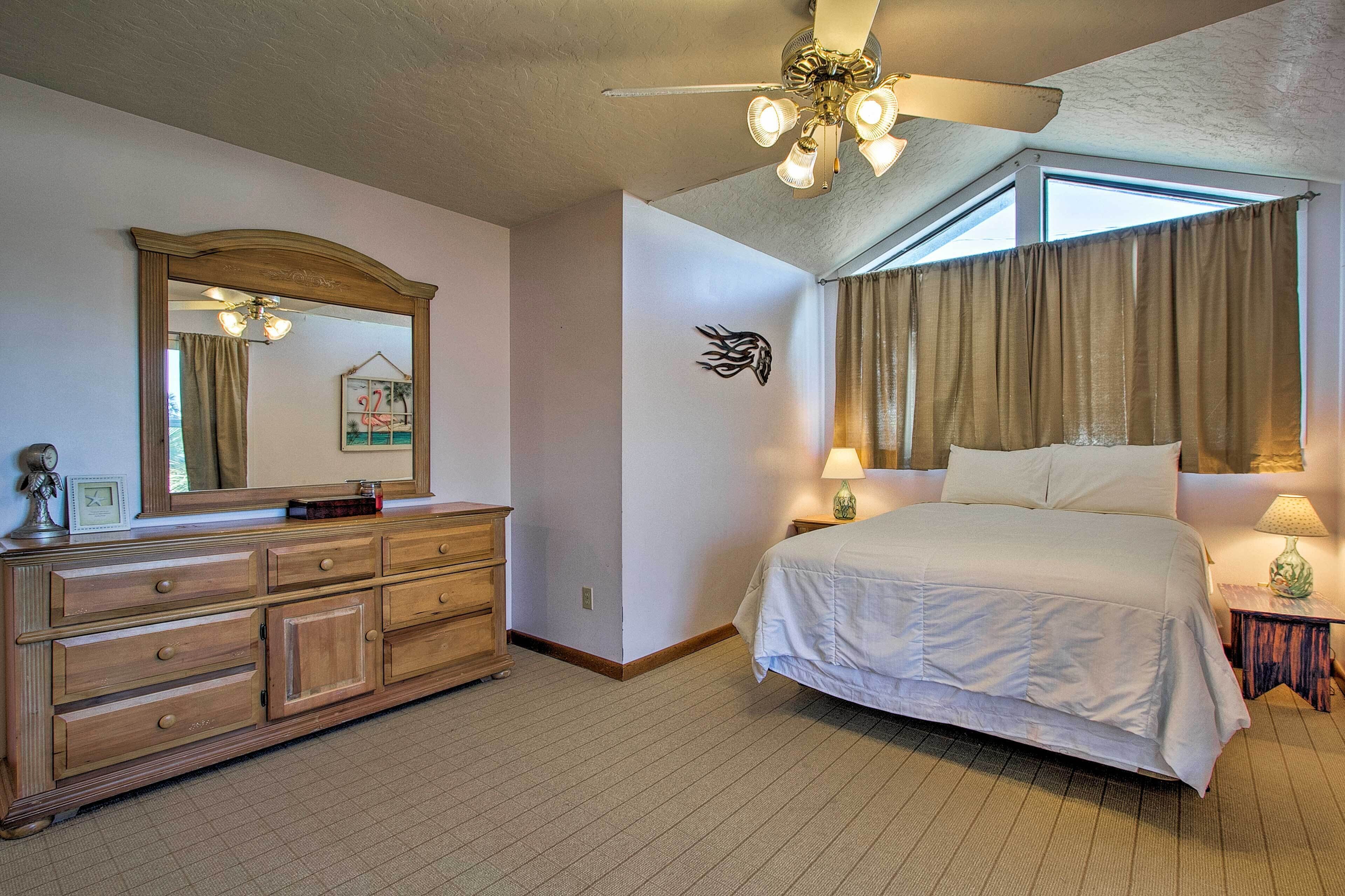 A hotel room with a large bed, a dresser, a ceiling fan, and a window with curtains.