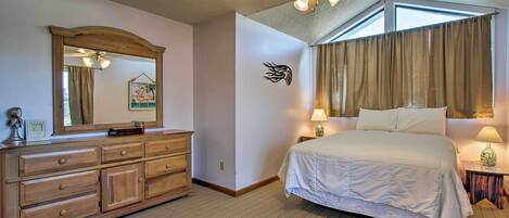 A hotel room with a large bed, a dresser, a ceiling fan, and a window with curtains.