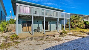Ein zweistöckiges Haus mit überdachter Terrasse, einem eingezäunten Garten und einem Sandstrand im Hintergrund.