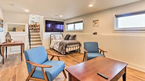 Une pièce confortable avec un lit, deux chaises bleues, une table en bois, un téléviseur et un escalier menant à un autre niveau.