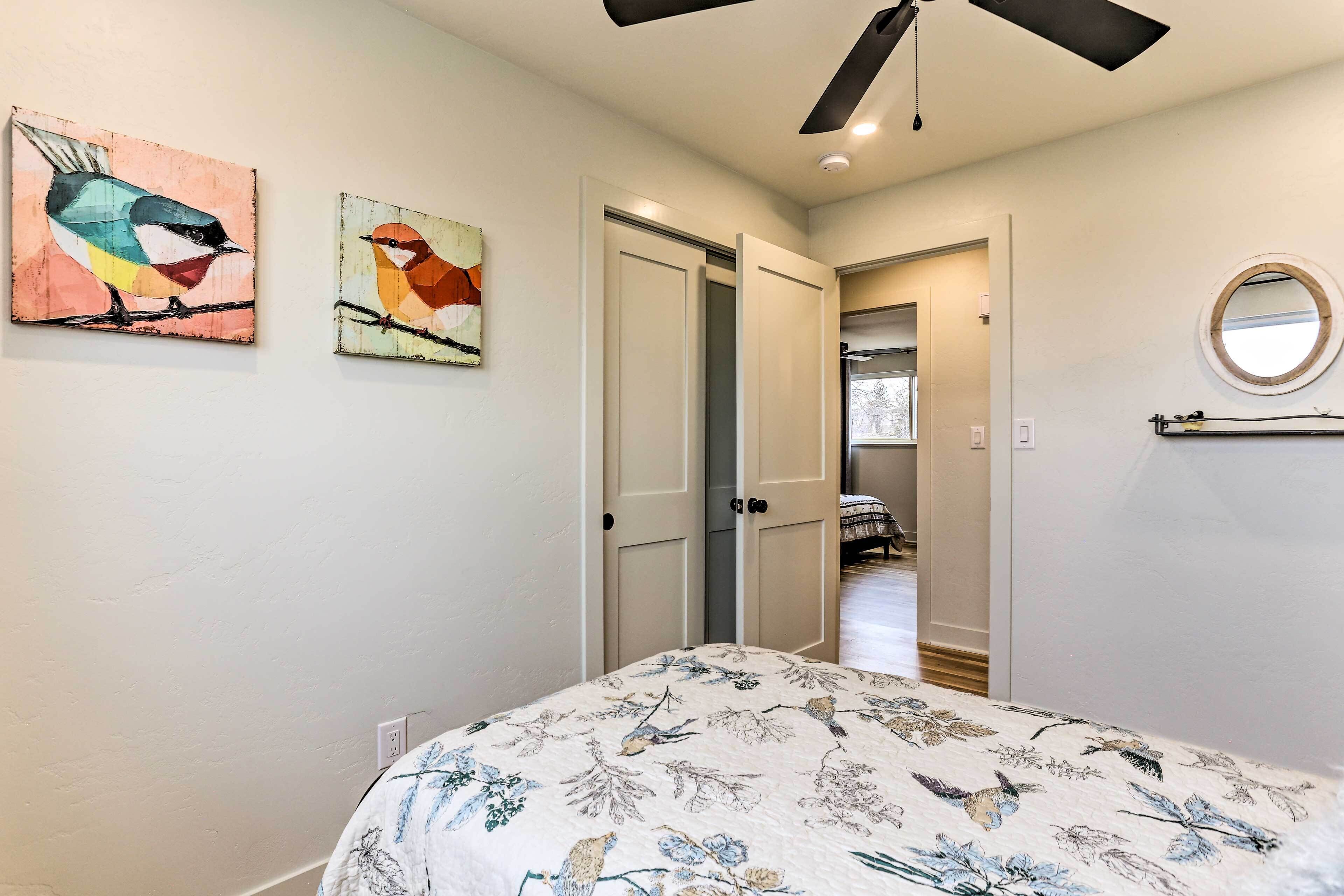 A bedroom with a bed, a ceiling fan, and two wall-mounted paintings of birds.
