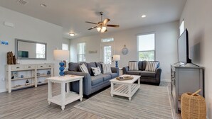 A modern living room with a ceiling fan, two sofas, a coffee table, a TV, and a bookshelf. - Coastal Port St Joe Getaway w/ Pool & Beach Access (Port St. Joe)
