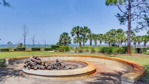 A circular outdoor fire pit surrounded by a curved stone border, with a grassy area and trees in the background. - Coastal Port St Joe Getaway w/ Pool & Beach Access (Port St. Joe)