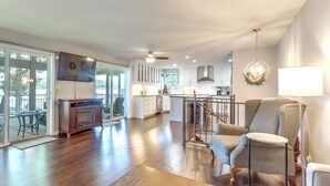 A spacious living area with a wooden floor, a comfortable armchair, a side table, and a view of the kitchen and dining area through glass doors. - Dock, Hot Tub! Family-friendly Camdenton Haven (Camdenton)
