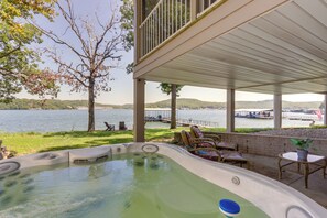 A hot tub area with a view of a lake, outdoor furniture, and a covered patio.