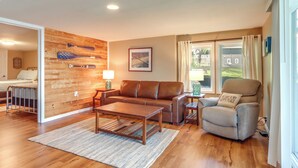 A modern living room with a wooden wall, a brown leather sofa, a wooden coffee table, and a recliner with a pillow. - Dock, Hot Tub! Family-friendly Camdenton Haven (Camdenton)