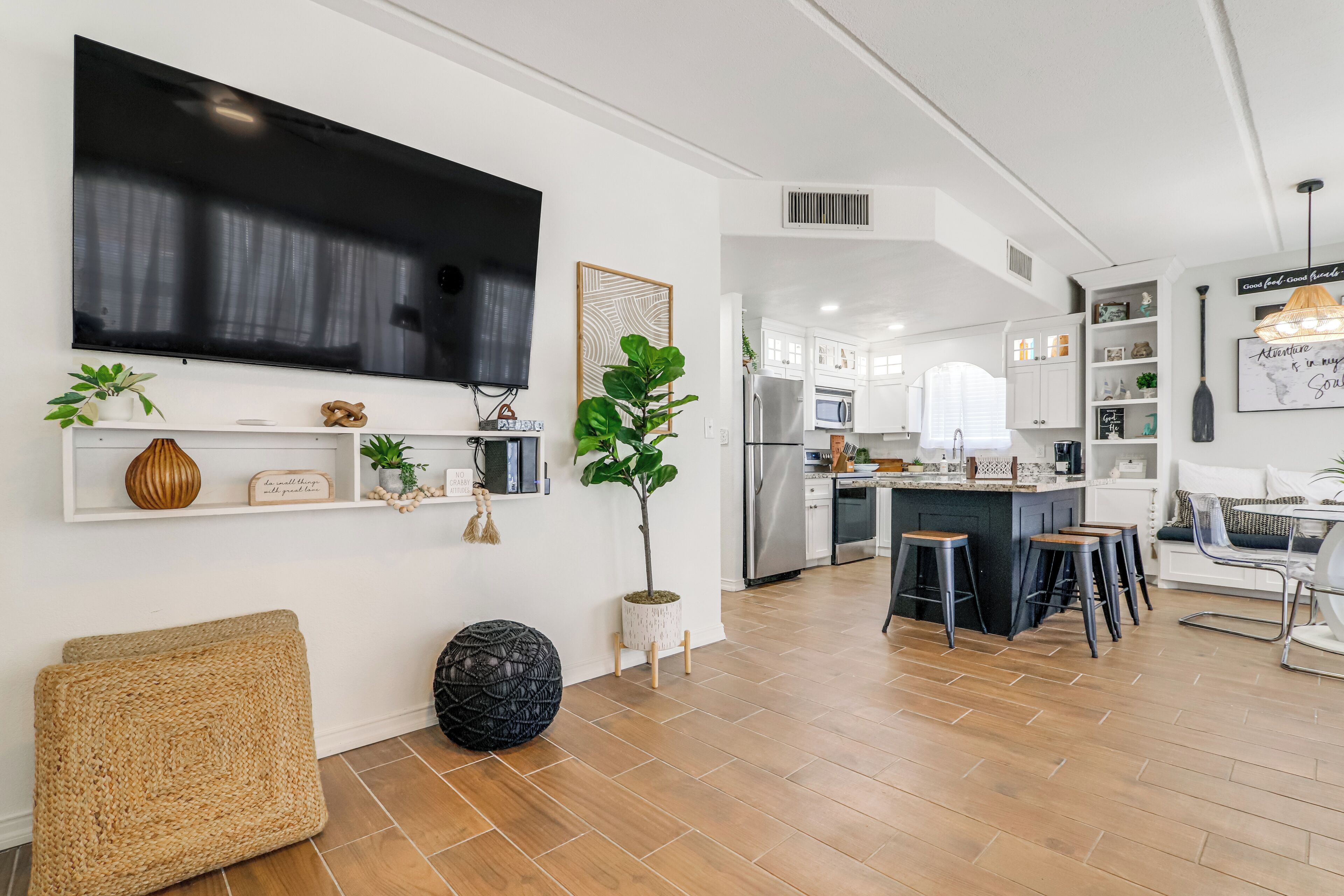 A modern kitchen with white cabinetry, a large flat-screen TV, and a dining area with stools.