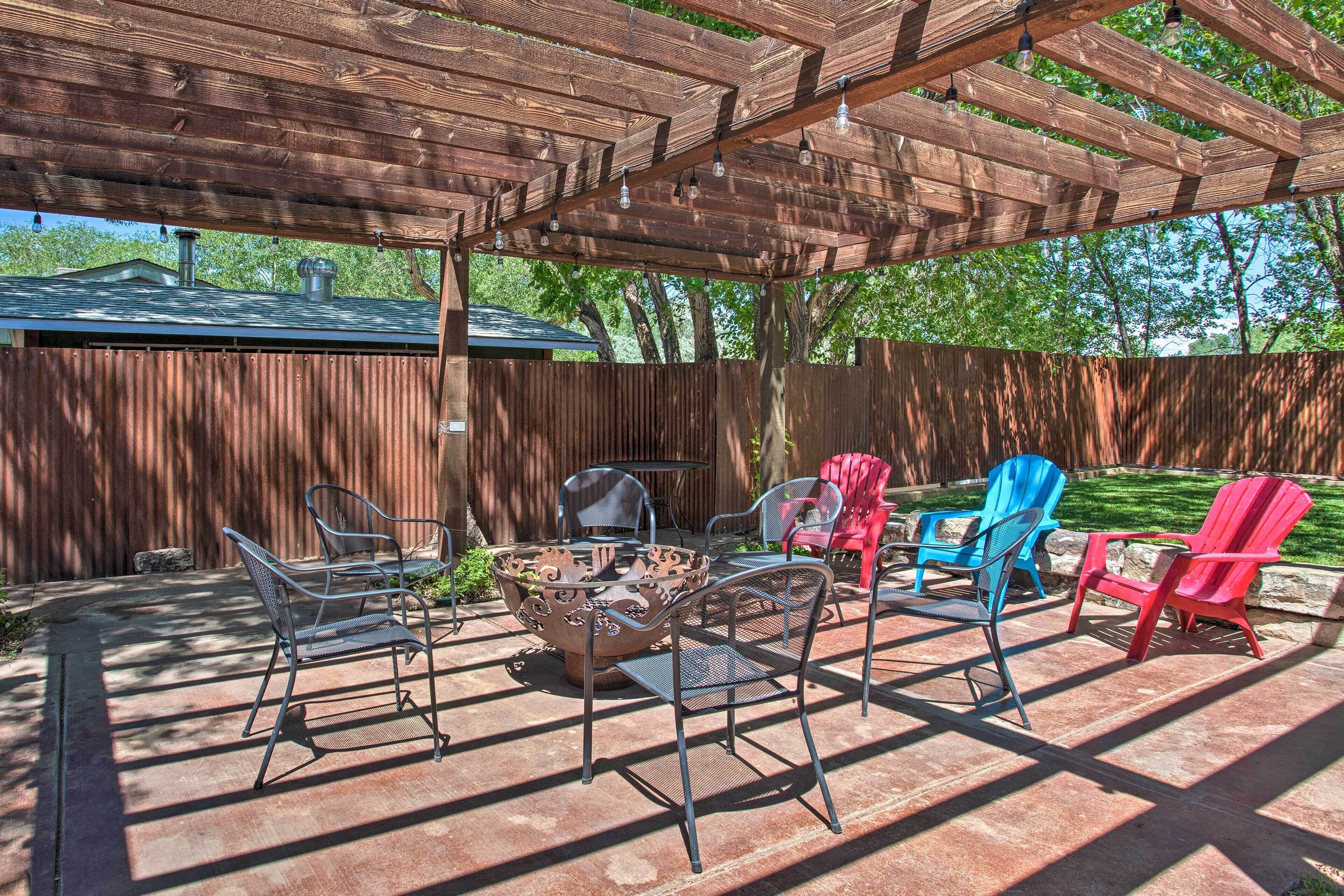 An outdoor patio with a pergola, metal chairs, a fire pit, and a wooden fence in the background.