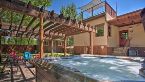 A hot tub area with a wooden pergola, outdoor seating, and a two-story house with a balcony. - Moab Getaway w/ Ample Parking, Walk to Main Street (Moab)