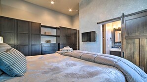 A bedroom with a large bed, dark wooden wardrobe, and a TV mounted on the wall. - Moab Getaway w/ Ample Parking, Walk to Main Street (Moab)