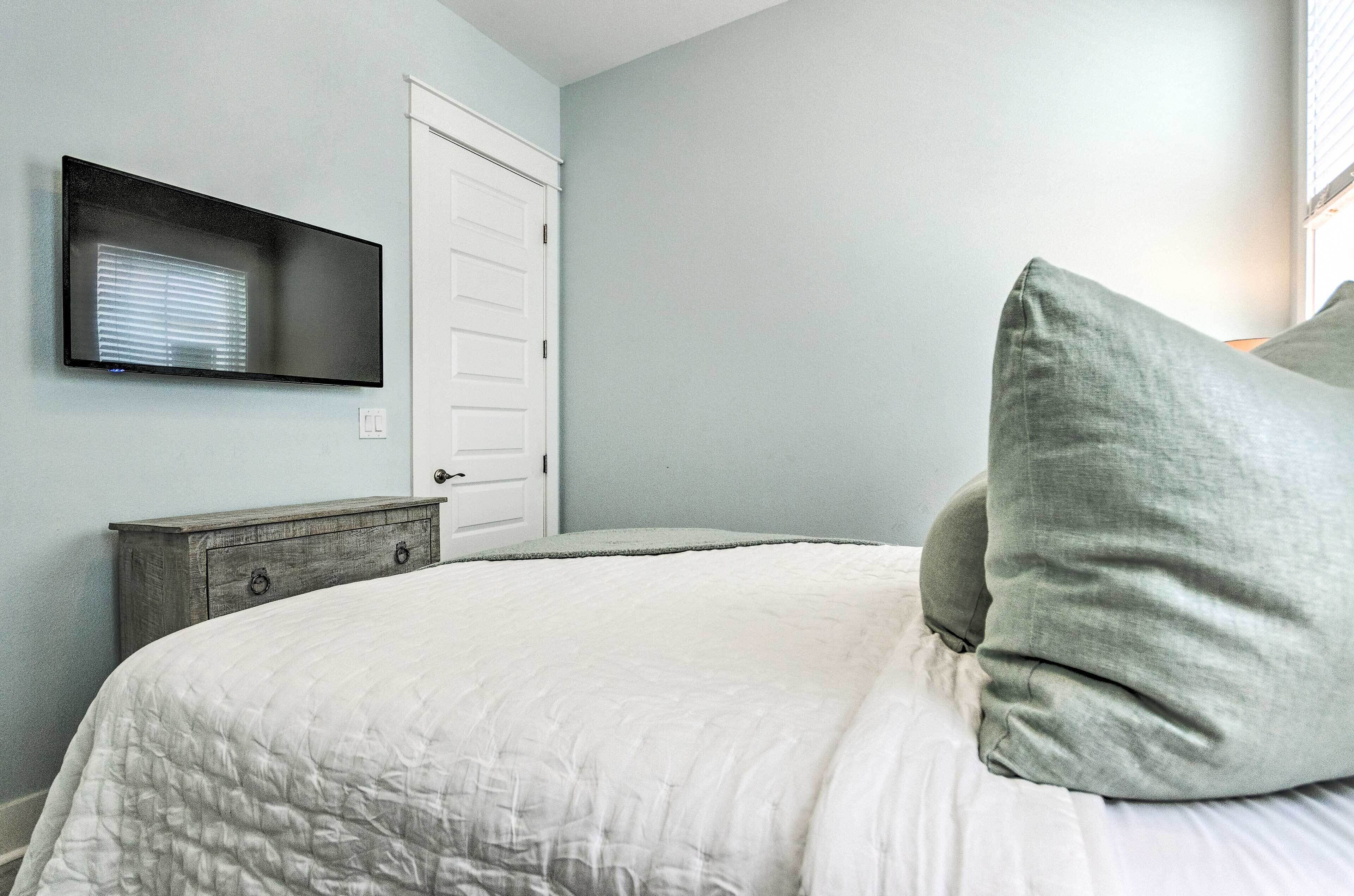 Een slaapkamer met een bed, een aan de muur bevestigde televisie, een deur en een houten dressoir.