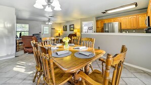 Un coin repas avec une table en bois dressée pour six personnes, entourée de chaises en bois. Un lustre est suspendu au-dessus, et deux lampes murales sont fixées au mur.
