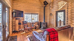 Interior de una cabaña de troncos con chimenea, sofá de cuero, estanterías de madera y televisor.