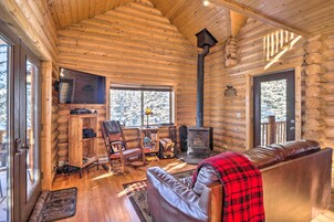 A log cabin interior with a fireplace, leather sofa, wooden shelves, and a television.