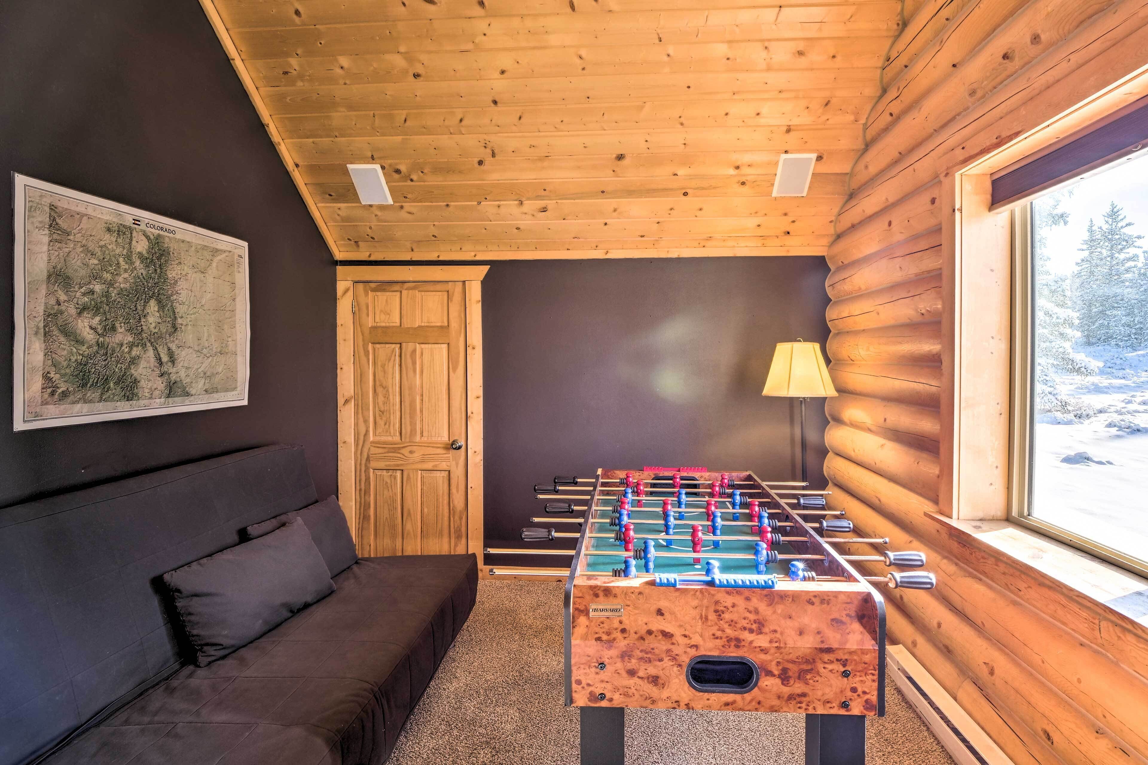 A cozy room with a foosball table, a sofa, a map on the wall, and a window with a snowy view.