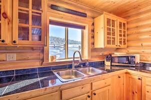 A wooden cabin kitchen with a double sink, a microwave, and cabinets.