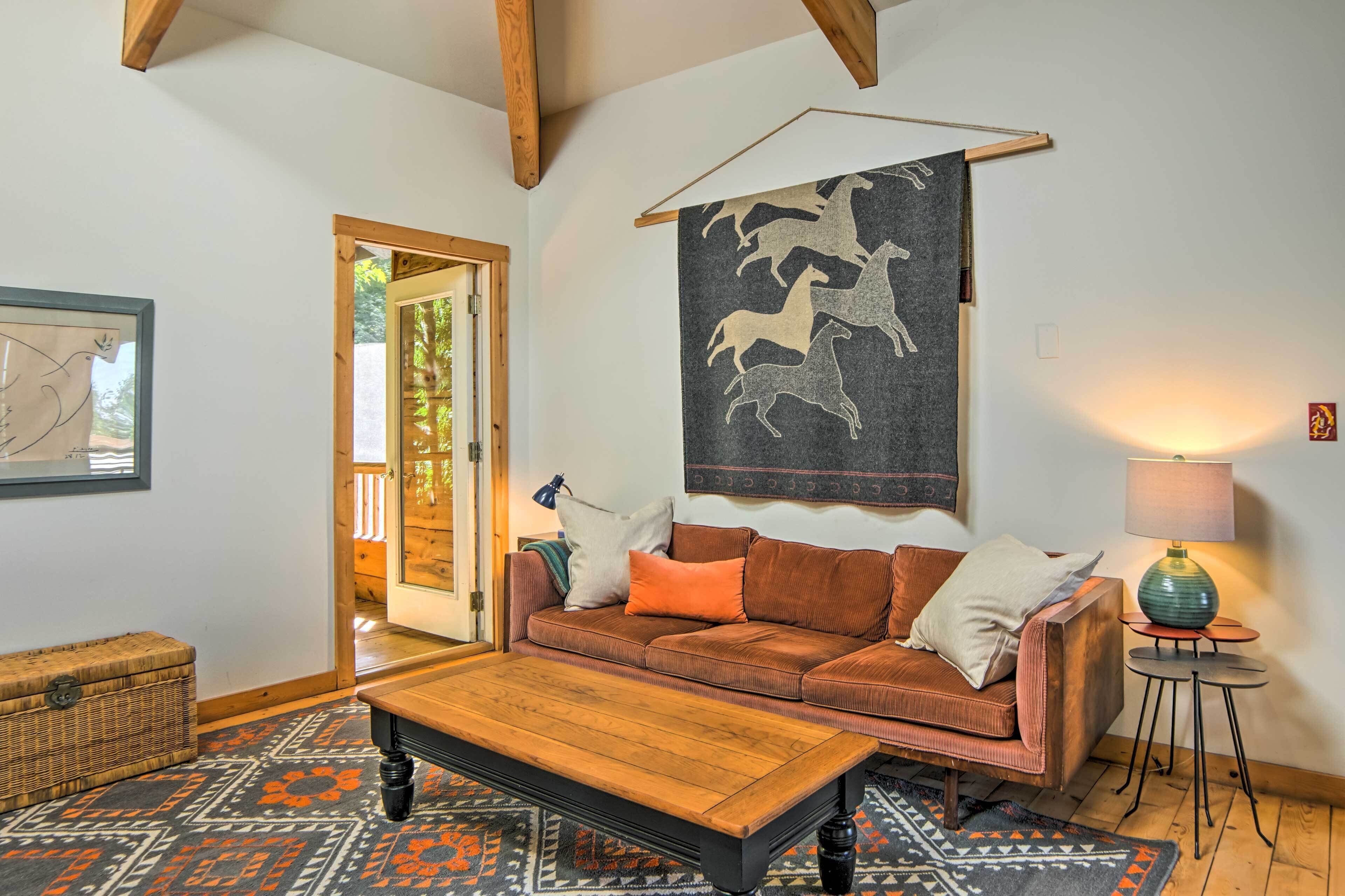 A cozy living room with a brown sofa, a wooden coffee table, patterned rug, and a tapestry of horses on the wall.