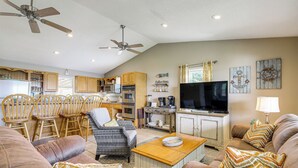 A spacious living room with a large brown leather sofa, a wooden coffee table, and a television. There are wooden chairs and a wicker chair in the background. - Rutledge Hilltop Home on Cherokee Lake w/ Decks! (Rutledge)