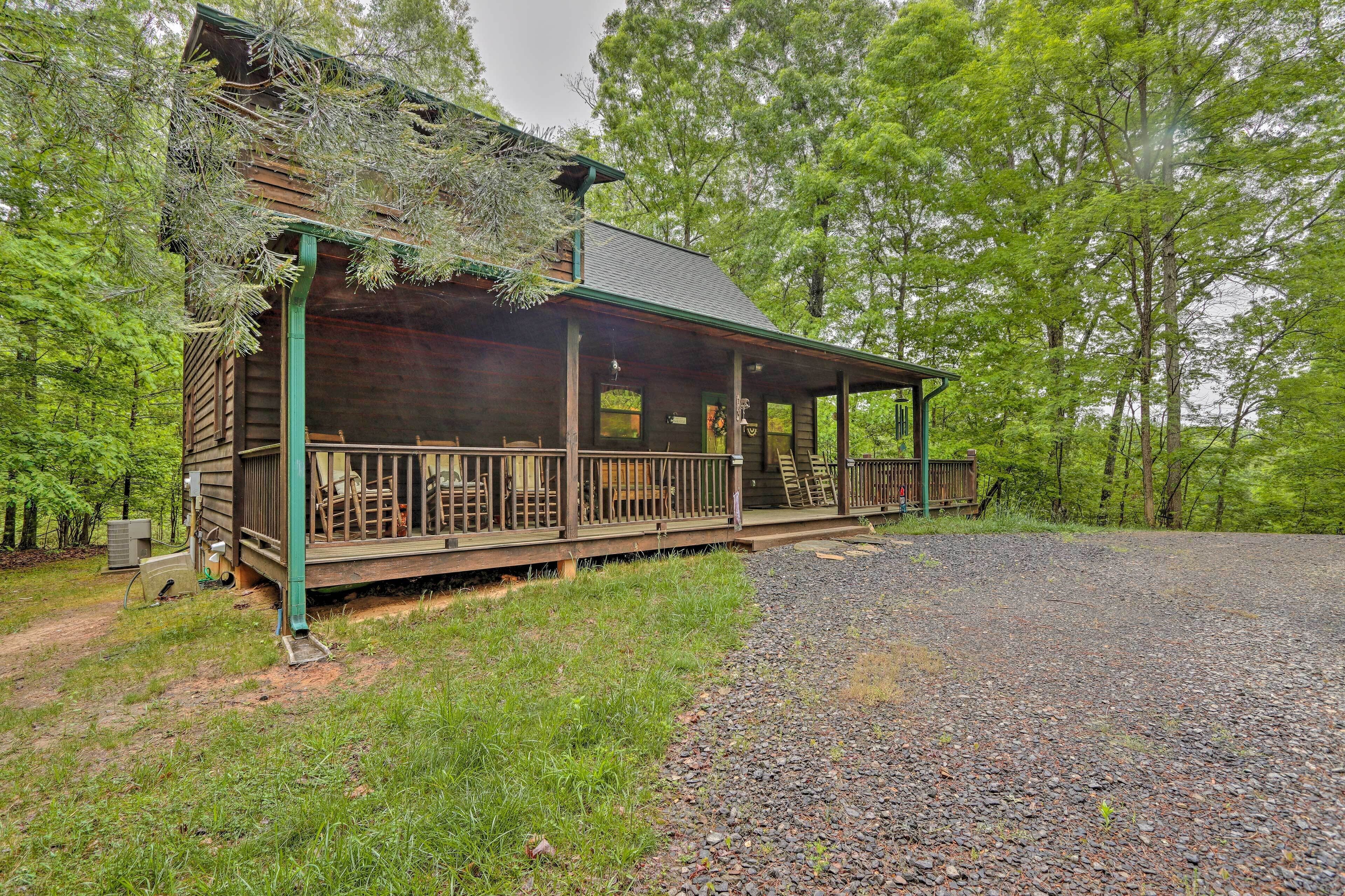 A wooden cabin with a porch, surrounded by trees.