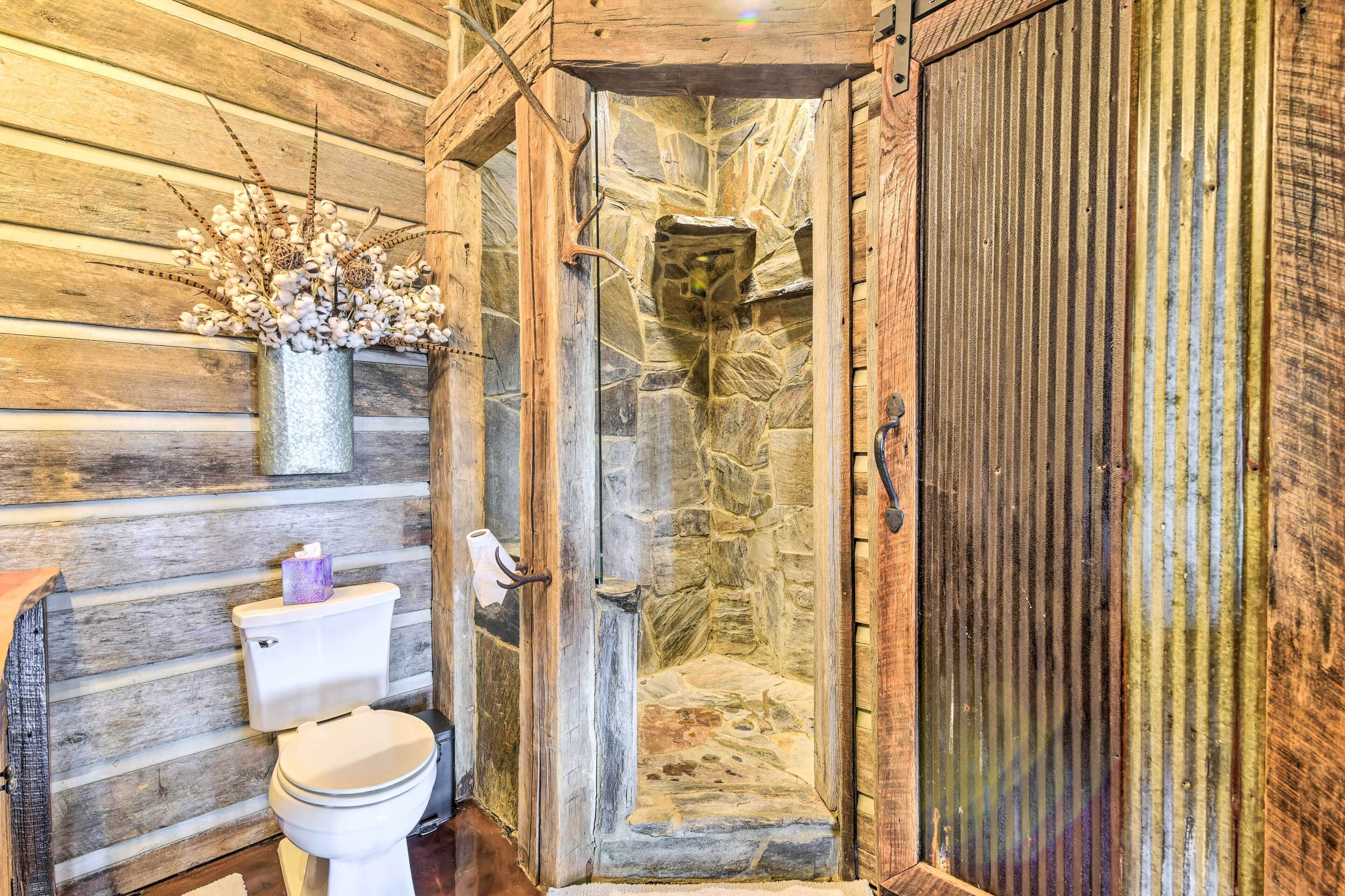 A rustic bathroom with a stone shower, wooden walls, and a toilet with a tissue box.