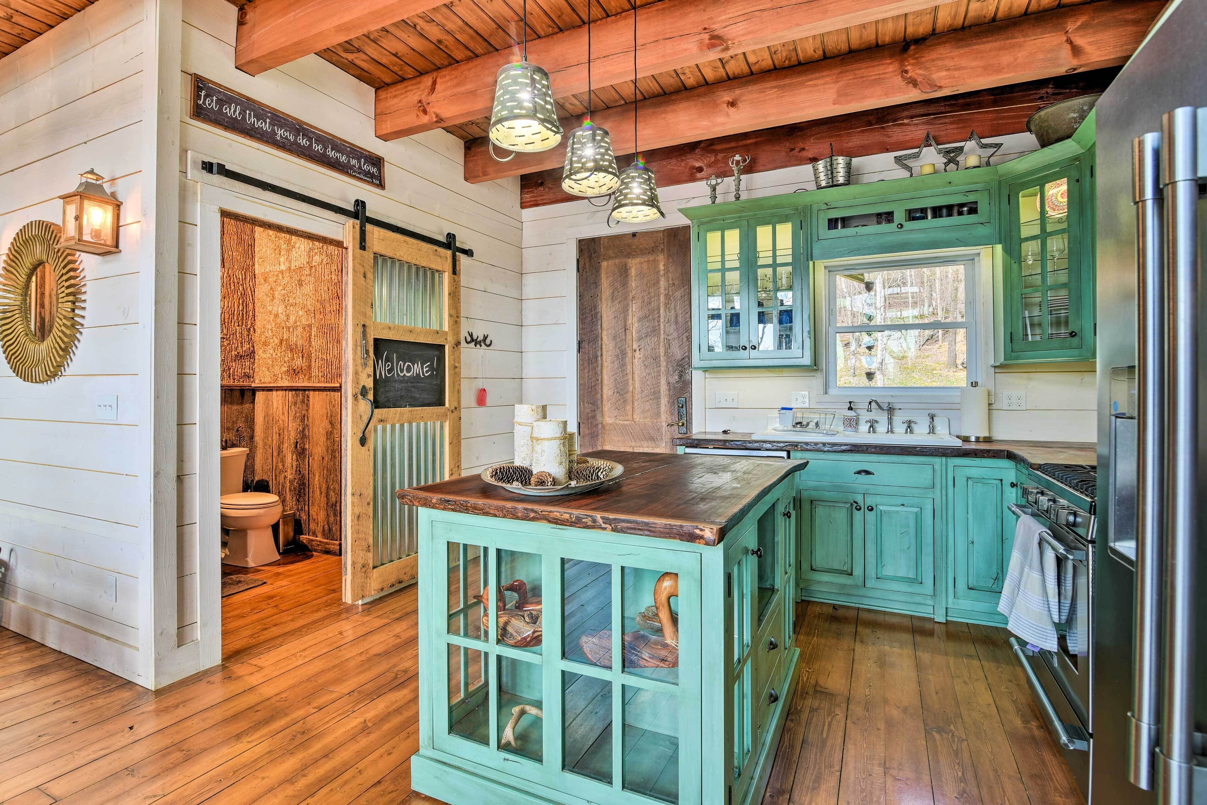A rustic kitchen with wooden floors, green cabinets, and a central island with glass doors.