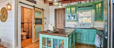 A rustic kitchen with wooden floors, green cabinets, and a central island with glass doors.