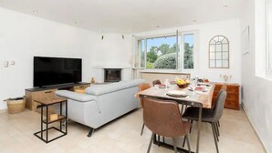 Un salon moderne doté d’un téléviseur à écran plat, d’un canapé, d’une table à manger avec des chaises et d’une cheminée.