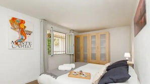 Une chambre à coucher avec un lit, une fenêtre avec des rideaux, une armoire en bois et un mur orné d’une affiche.