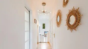 Un couloir doté d’un sol carrelé de couleur claire, d’un luminaire au plafond et de deux miroirs décoratifs fixés au mur.