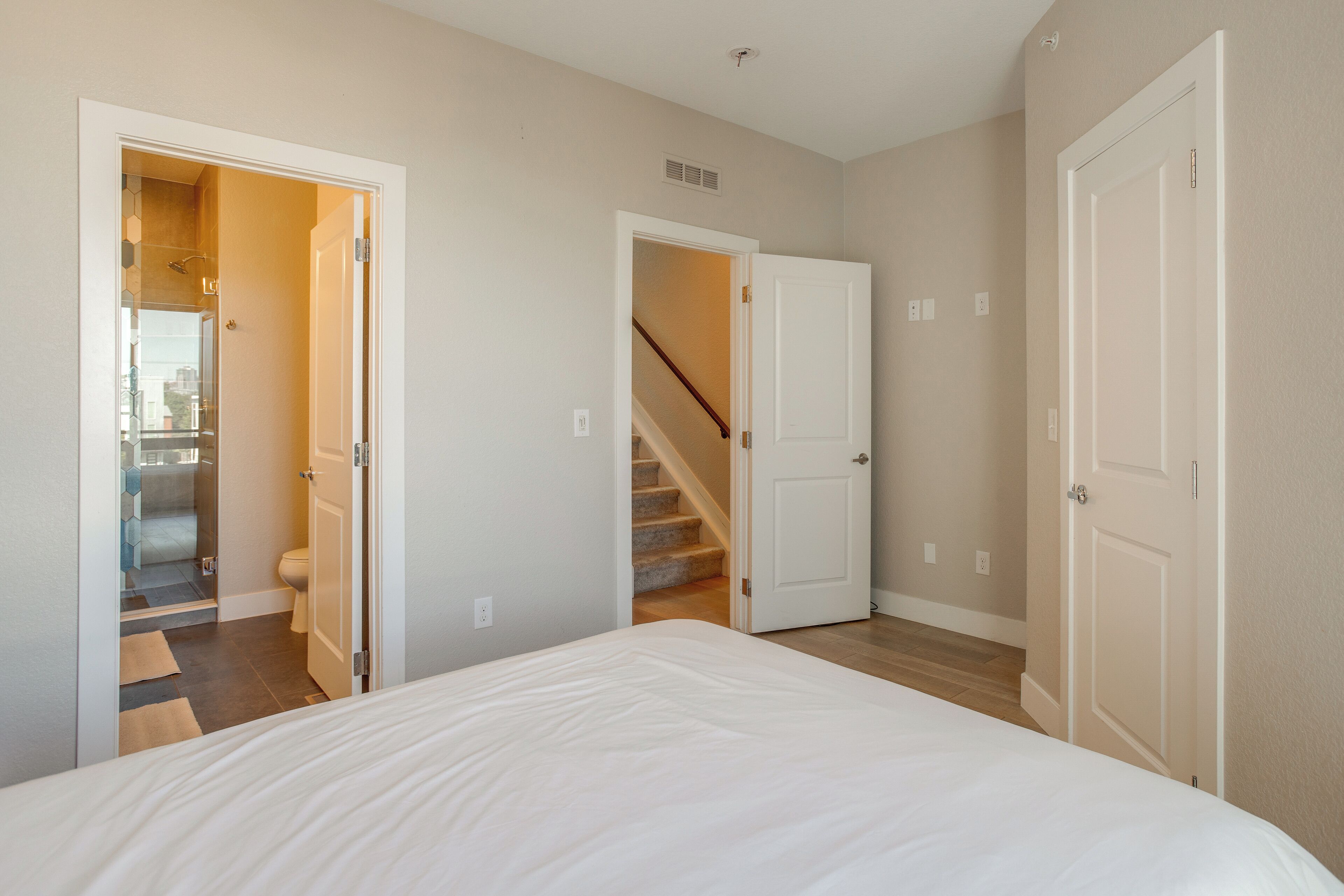 A bedroom with a large bed, a bathroom with a shower, and a staircase leading to another room.