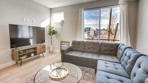 A modern living room with a large flat-screen TV, a grey sectional sofa, a glass coffee table, and a wooden TV stand. - Mountain-view Rooftop Deck: Denver Townhome (Denver)