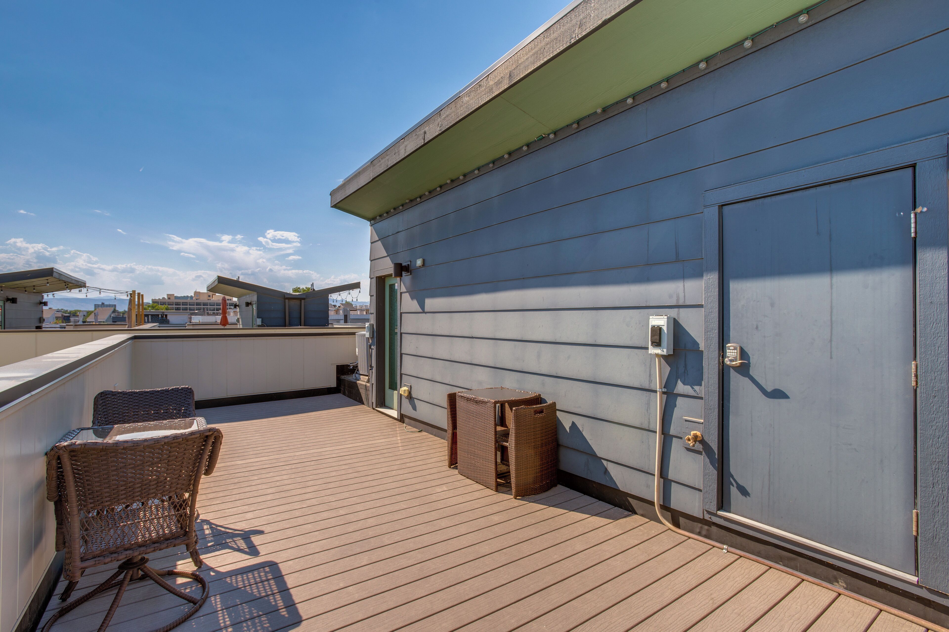 A rooftop terrace with a wicker chair, a small table, and a door.