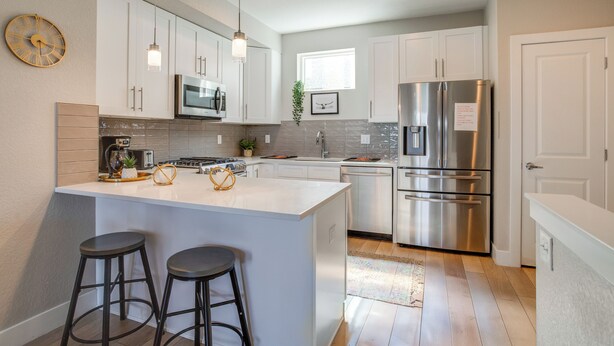 A modern kitchen with white cabinetry, stainless steel appliances, a large island with stools, and pendant lighting. - Mountain-view Rooftop Deck: Denver Townhome (Denver)