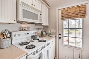 Una cocina con armarios blancos, un microondas, una estufa y un ventanal con persiana de madera.