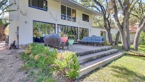 A two-story house with large windows, a covered patio with outdoor furniture, and a well-maintained garden. - Modern Austin Home w/ Yard ~ 1 Mi From Acl! (Austin)